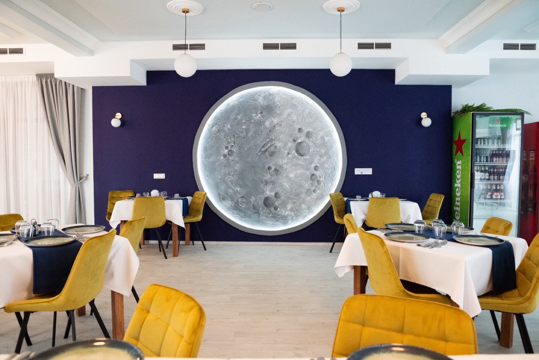 Salonul restaurantului FullMoon by Magnolia, cu luna luminoasă de pe peretele indigo și scaune de catifea muștar
