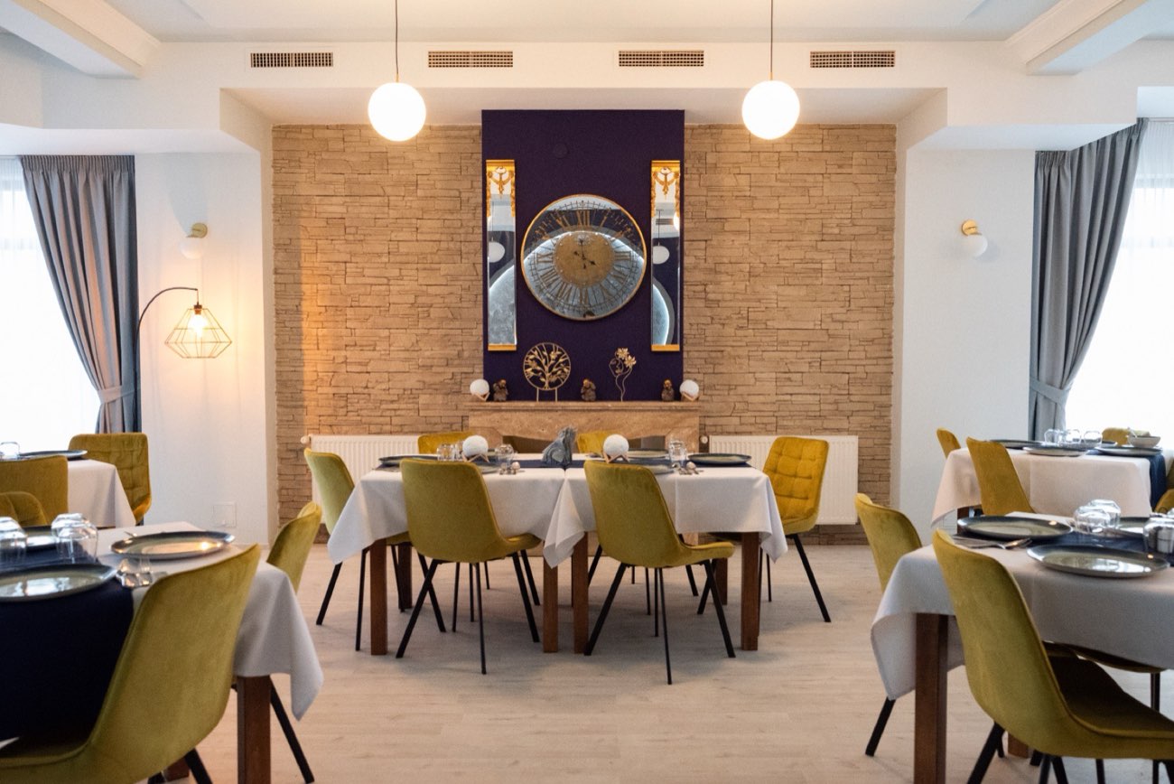 Sala de mese cu peretele indigo, ceasul auriu și scaune de catifea muștar